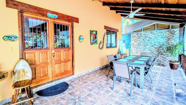 A patio area with a wooden door, a table with chairs, a ceiling fan, and a stone wall. - Stylish & Cozy Private Rooms in Tropical Paradise (Playa Herradura)