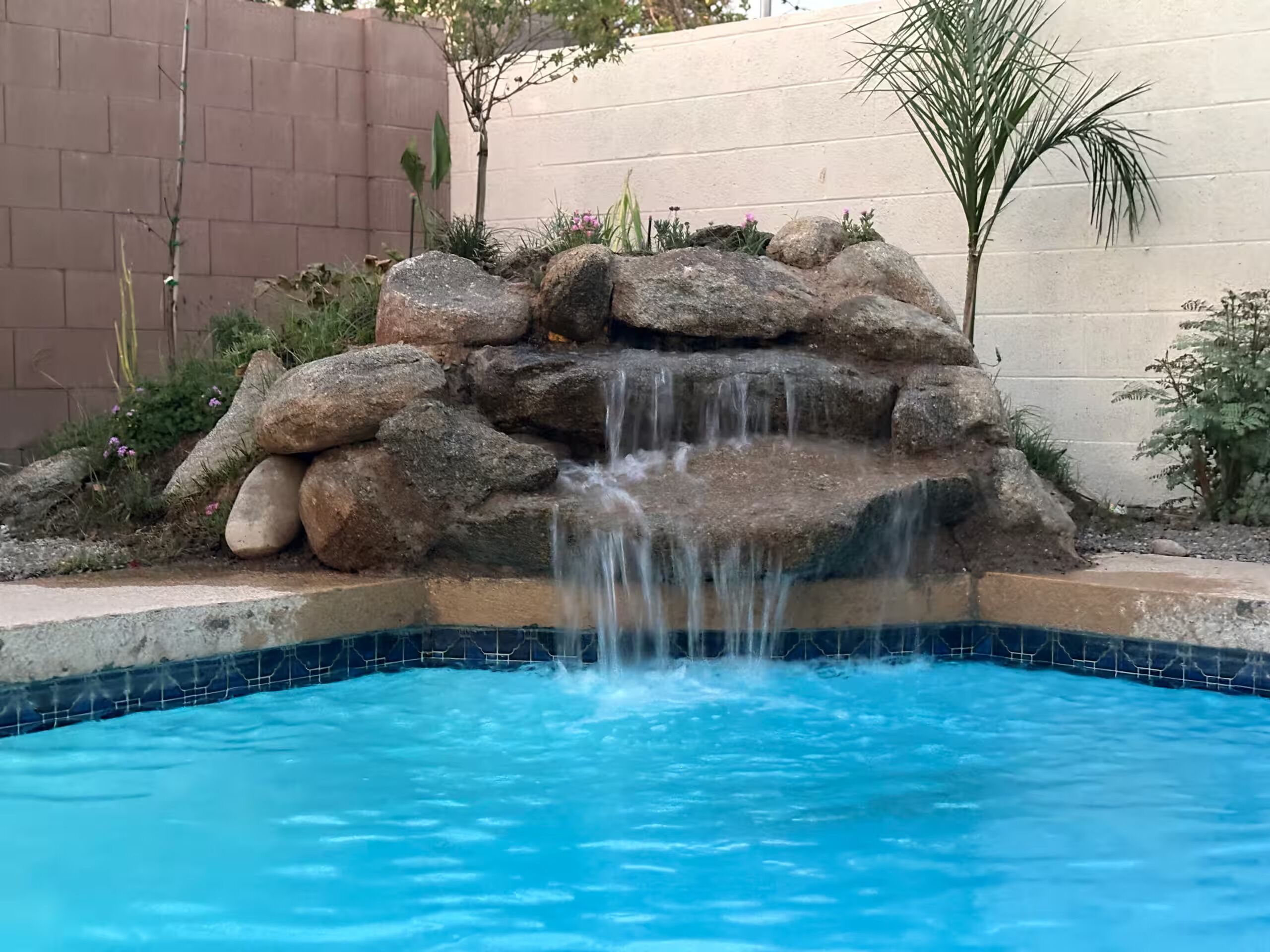 Ein Swimmingpool mit Wasserfall, umgeben von Steinen und Pflanzen.