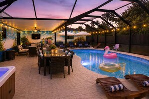 Área externa com piscina, mesa de jantar, espreguiçadeiras e banheira de hidromassagem.