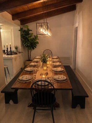 Une salle à manger avec une longue table en bois dressée pour un repas, agrémentée de bougies et d’un luminaire suspendu.