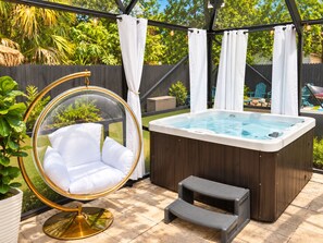 Ein Whirlpool mit Holzverkleidung, ein Hängestuhl mit goldfarbener Umrandung und eine kleine Treppe.