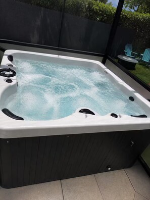 Un bain à remous avec une structure extérieure en bois, un siège intégré et un panneau de commande.