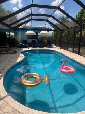 Une piscine dotée d’une structure en verre, de chaises longues et d’un flotteur en forme de flamant rose.