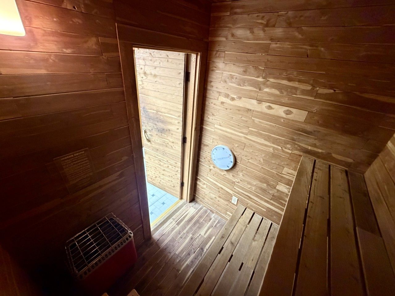 Un intérieur en bois avec une porte donnant sur l’extérieur, une petite fenêtre et une horloge fixée au mur.
