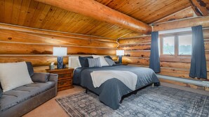 A log cabin bedroom with a bed, bedside tables, a sofa, and a window with curtains. - Chena Riverside Lodge (Fairbanks)
