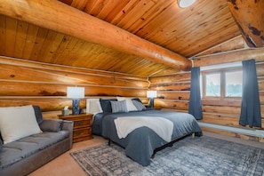 A log cabin bedroom with a bed, bedside tables, a sofa, and a window with curtains. - Chena Riverside Lodge (Fairbanks)