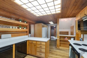 A compact kitchen with wooden cabinets, a built-in dishwasher, and a stove. - Chena Riverside Lodge (Fairbanks)