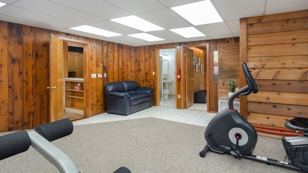 A room with a treadmill, a black leather sofa, wooden walls, and a visible bathroom. - Chena Riverside Lodge (Fairbanks)
