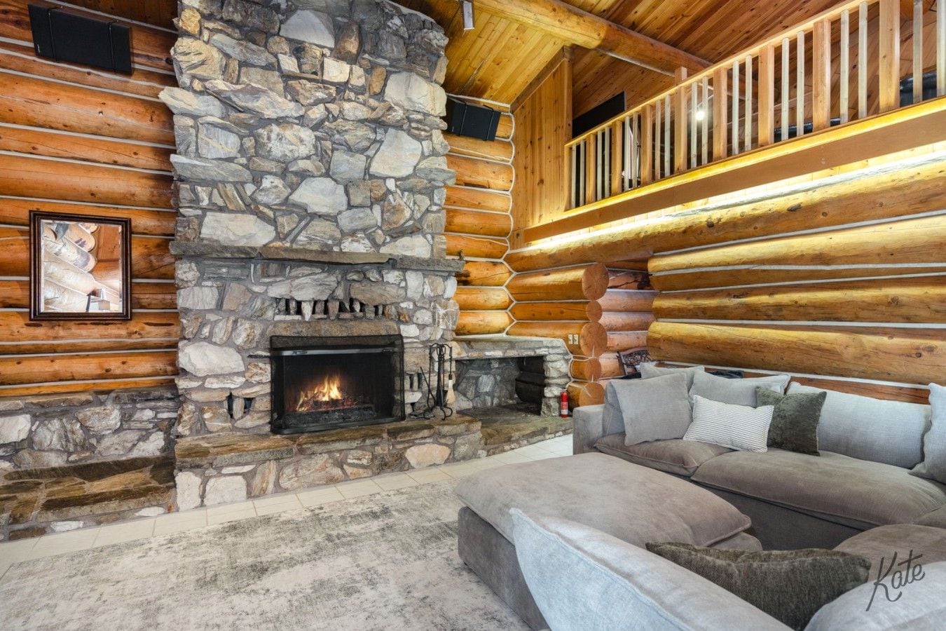 A log cabin interior with a stone fireplace, a sofa, and a wooden staircase.
