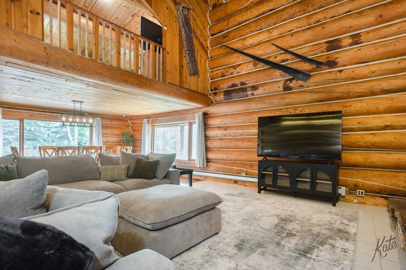 A log cabin interior with a sectional sofa, a flat-screen TV, and a dining area with wooden furniture.