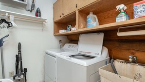 A laundry area with a washing machine, a vacuum cleaner, and cleaning supplies on shelves. - Chena Riverside Lodge (Fairbanks)