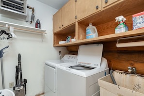 A laundry area with a washing machine, a vacuum cleaner, and cleaning supplies on shelves. - Chena Riverside Lodge (Fairbanks)