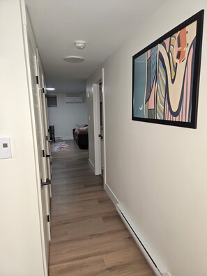 Ein Korridor mit Holzboden, einer Tür links und einem farbenfrohen, abstrakten Gemälde an der rechten Wand.
