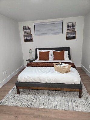 Quarto com cama, mesa de cabeceira, luminária e quadros nas paredes.