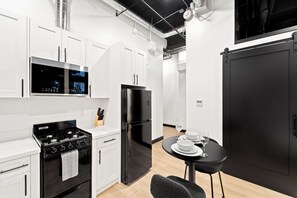 Een moderne keuken met witte kastjes, een zwarte koelkast, een fornuis en een magnetron. Er staat een eettafel met borden en een wijnglas.