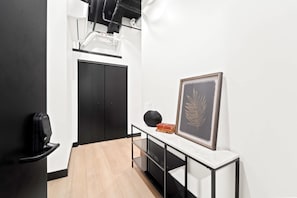 A hallway with a black door, a framed plant, and a black speaker on a white console table. - Your Downtown Base | Walk to Petco Park & Gaslamp! (San Diego)