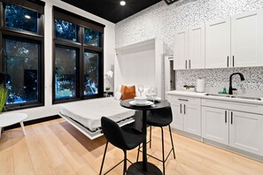 Un dormitorio moderno con cama, mesita de noche y ventana con vistas a árboles.