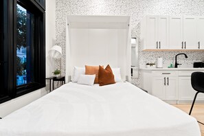 Een moderne slaapkamer met een groot bed, een nachtkastje, een lamp en uitzicht op het omliggende landschap.