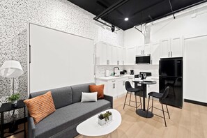 A modern kitchen with white cabinets, a black refrigerator, and a dining area with a white table and two black chairs. - Your Downtown Base | Walk to Petco Park & Gaslamp! (San Diego)
