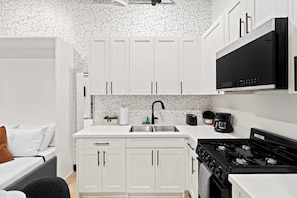 A modern kitchen with white cabinets, a black stove, and a coffee maker. - Your Downtown Base | Walk to Petco Park & Gaslamp! (San Diego)