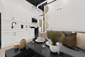 Eine moderne Küche mit weißen Schränken, einer schwarzen Arbeitsplatte und einem schwarzen Herd. Es gibt eine schwarze Kaffeemaschine, eine Mikrowelle und ein Spülbecken.