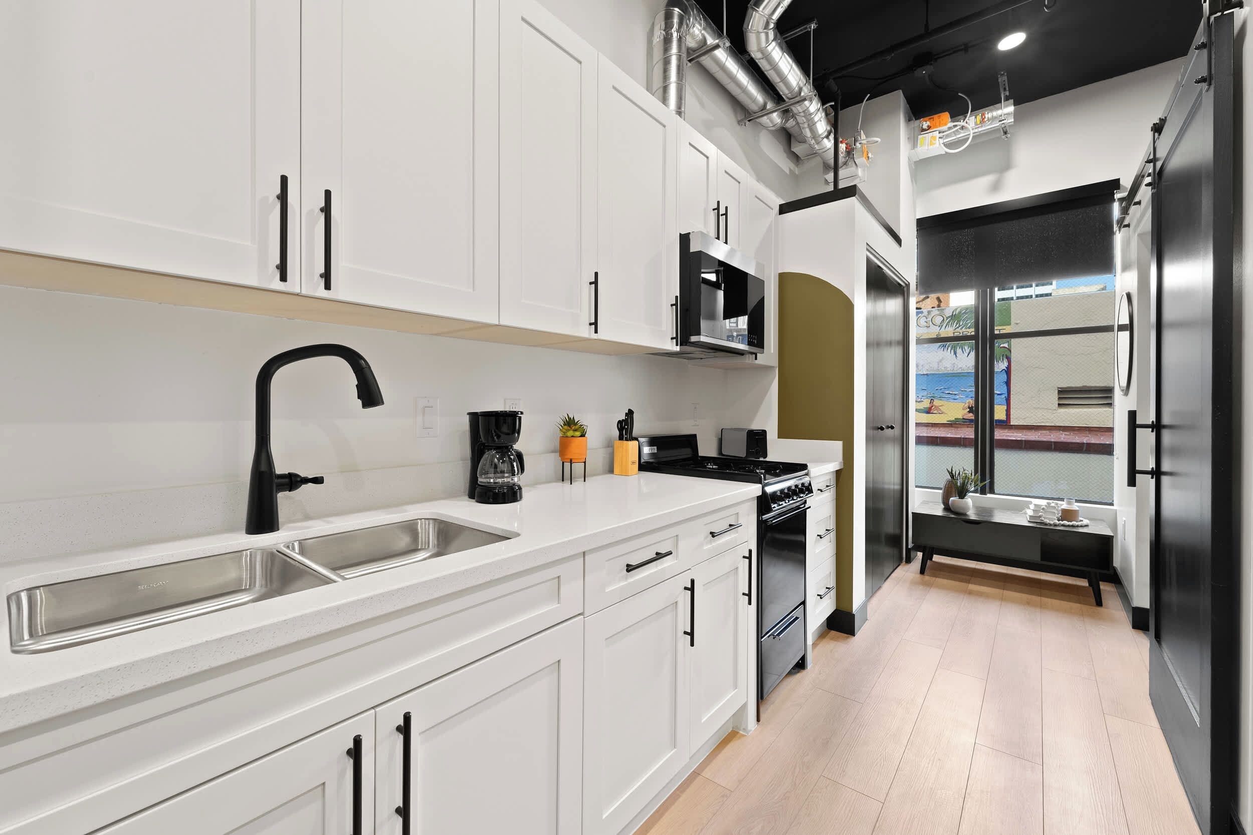 A modern kitchen with white cabinetry, a black faucet, a coffee maker, and a stove.