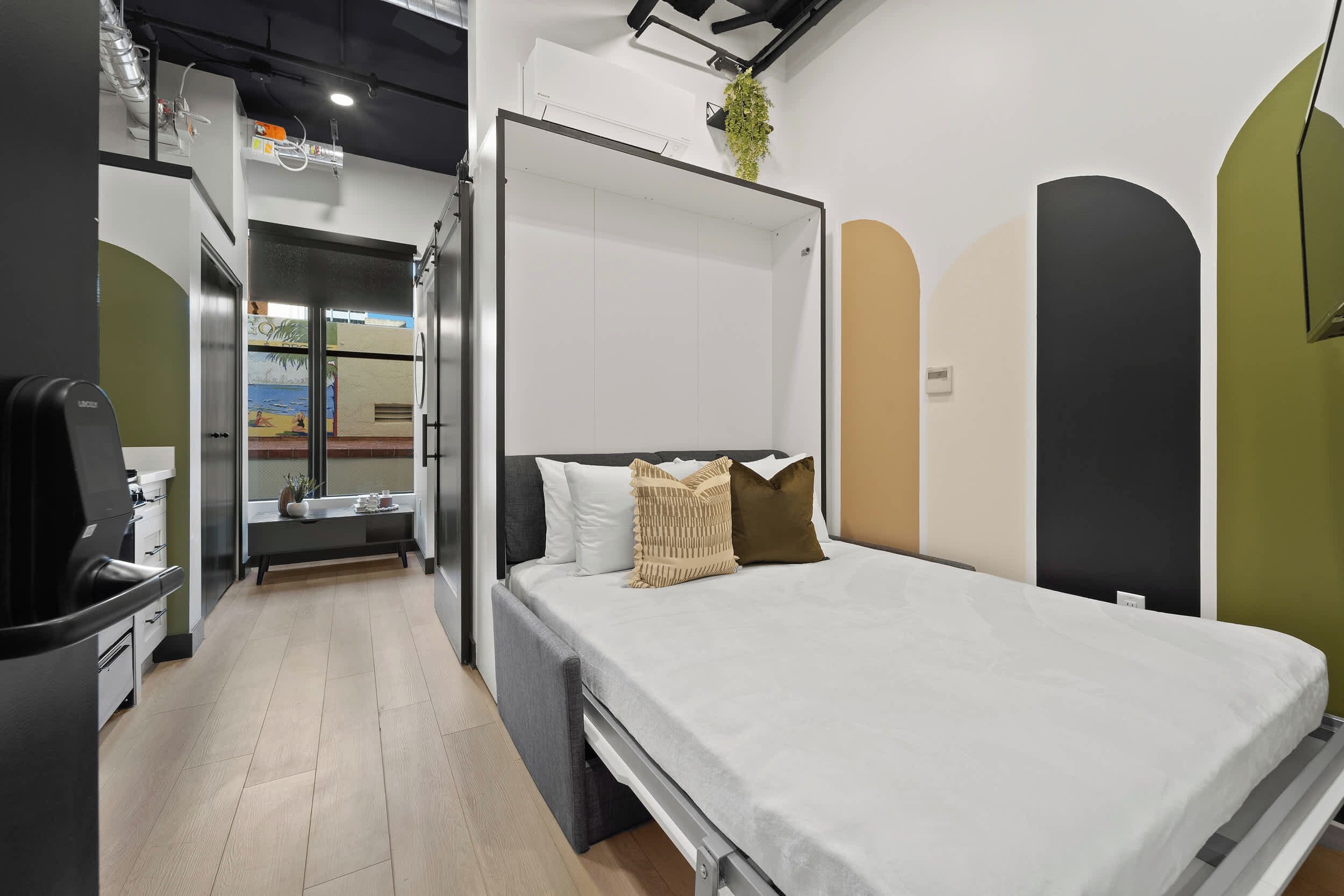 A modern hotel room with a bed, a desk, and a view of the city.