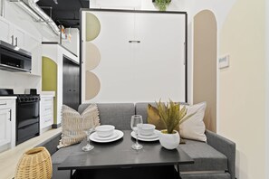 Een moderne keuken met een eethoek, inclusief een fornuis, oven en een tafel gedekt voor twee personen, met borden, glazen en een plant.