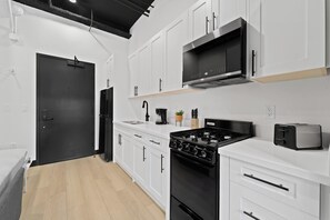 Een moderne keuken met witte kasten, een zwarte kookplaat en een magnetron boven de spoelbak.