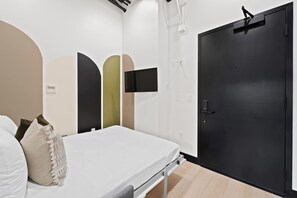 Ein Hotelzimmer mit einem Bett, einer schwarzen Tür und einem an der Wand befestigten Fernseher.