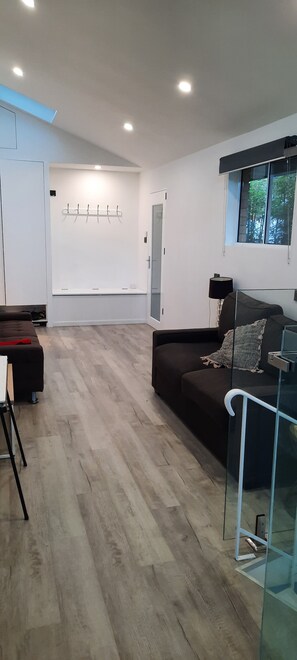 A modern living room with a dark sofa, a glass coffee table, and a view of the outdoors through a window. - Family home walking distance to Terrigal beach (Terrigal)