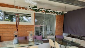 Ein moderner Außenbereich zum Sitzen mit einem Glastisch und Stühlen, einer Ziegelwand und einem Fenster mit Blick auf Bäume.