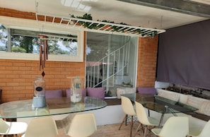 A modern outdoor seating area with a glass table and chairs, a brick wall, and a window with a view of trees. - Family home walking distance to Terrigal beach (Terrigal)