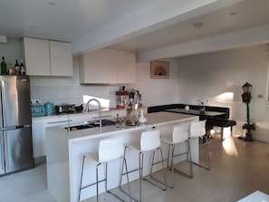A modern kitchen with a central island, bar stools, and a coffee machine. - Family home walking distance to Terrigal beach (Terrigal)