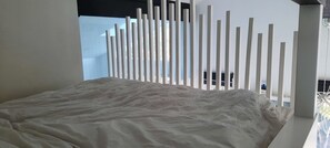 A bed with a textured white cover, a white wall with vertical slats, and a view of the outdoors through a window. - Family home walking distance to Terrigal beach (Terrigal)
