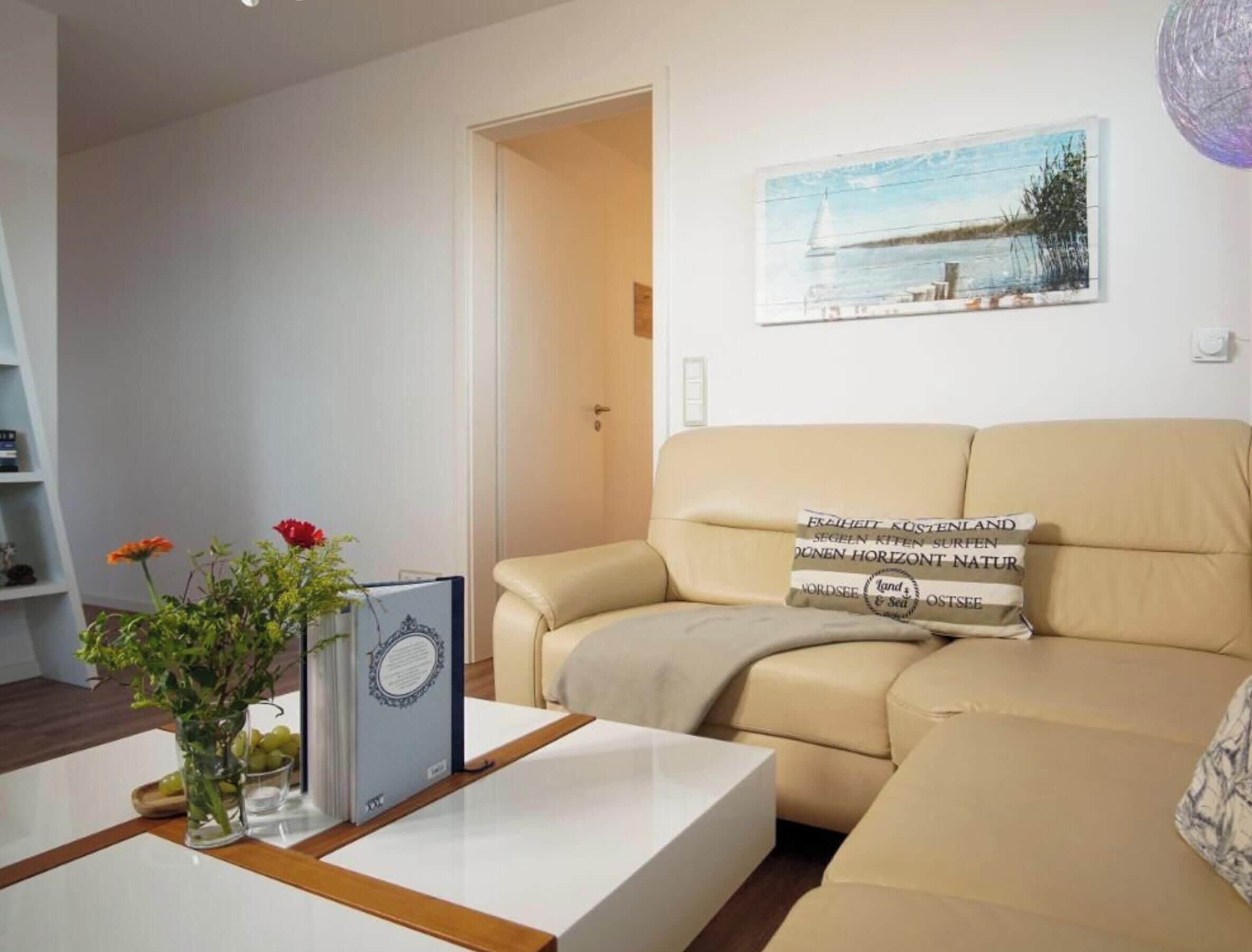 Una sala de estar con un sofá color beige, una mesa de centro blanca y un certificado enmarcado.