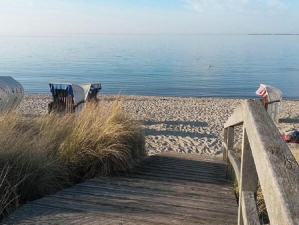 A wooden boardwalk leading to a sandy beach with calm water in the background. - Holiday Apartment With 1 Bedroom (Heiligenhafen)
