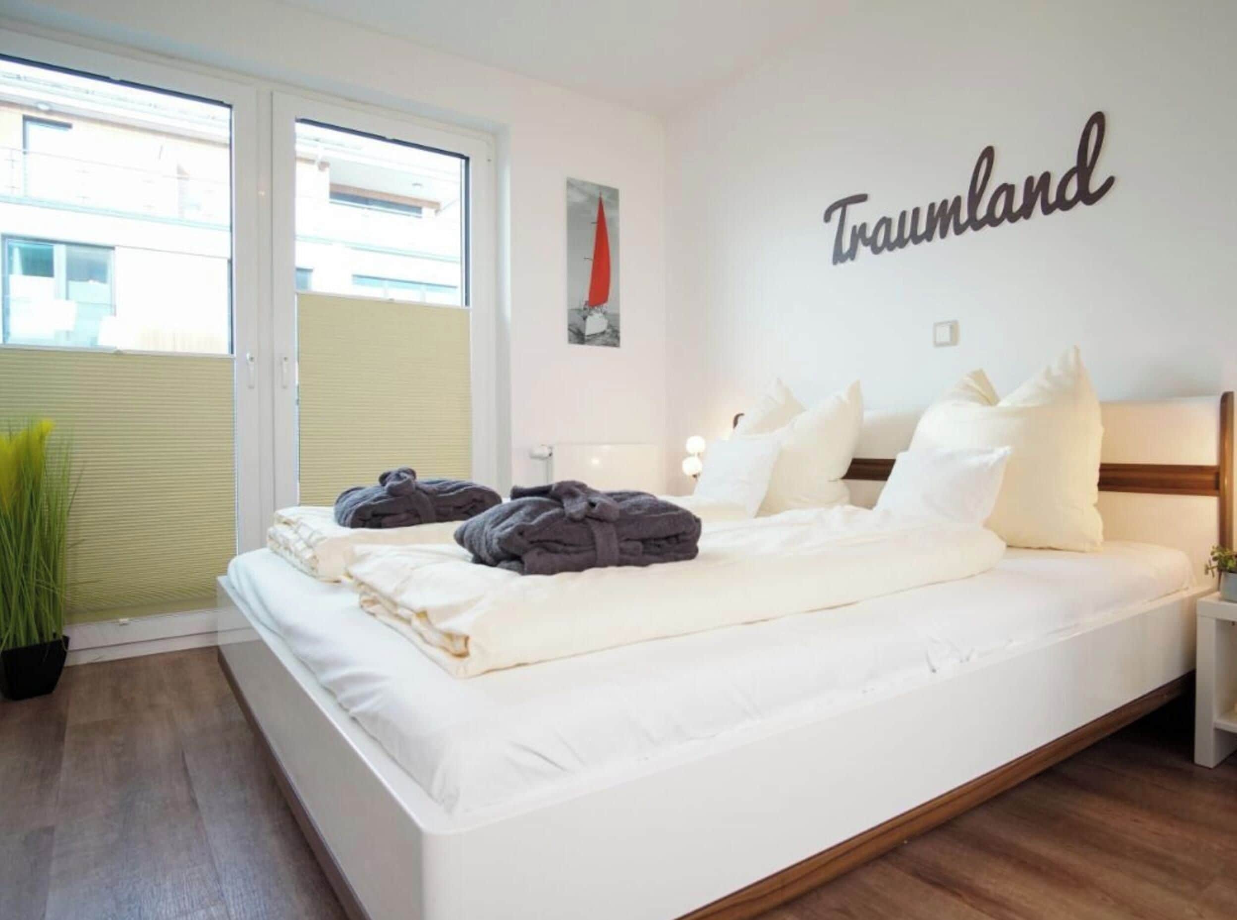 Quarto com cama, janela, parede com a palavra 'Traumland' e uma planta.