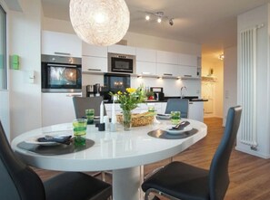 A modern kitchen with white cabinets, a built-in oven, and a hanging light fixture. - Holiday Apartment With 1 Bedroom (Heiligenhafen)