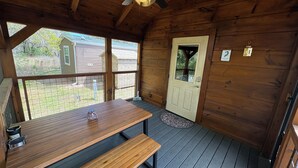 Una cabaña de madera con una mesa de comedor y bancos, un ventilador de techo y una puerta con ventana.