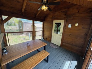 Eine Holzhütte mit Esstisch und Bänken, einem Deckenventilator und einer Tür mit Fenster.