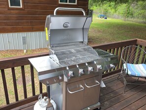 Una parrilla portátil sobre una terraza de madera, con una silla metálica y una mesa de picnic al fondo.