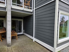 A two-story building with a balcony, a sliding glass door, and a patio area with a table and chairs. - Oceanside Garden Studio B: Pool & Hot tub (Nanoose Bay)