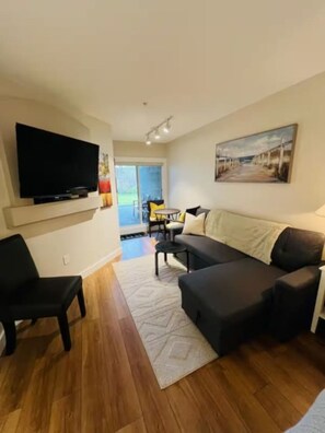 A living room with a flat-screen TV, a sofa, a coffee table, and a rug. - Oceanside Garden Studio B: Pool & Hot tub (Nanoose Bay)