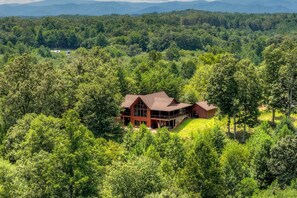 A large, two-story cabin surrounded by dense forest, with a clear view of the surrounding landscape. - Blue Ridge Retreat on Wolf Creek - Hot Tub, Game Room, Firepit + EV Charger (Mineral Bluff)