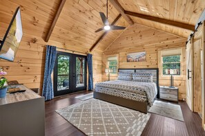 A wooden cabin bedroom with a bed, a desk, a chair, a window, and a ceiling fan. - Blue Ridge Retreat on Wolf Creek - Hot Tub, Game Room, Firepit + EV Charger (Mineral Bluff)