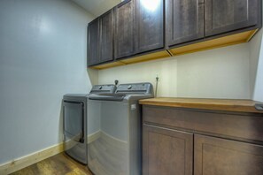 A laundry room with a washing machine and dryer, wooden cabinets, and a light switch on the wall. - Blue Ridge Retreat on Wolf Creek - Hot Tub, Game Room, Firepit + EV Charger (Mineral Bluff)