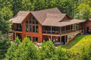 A two-story wooden cabin with a large deck and hot tub. - Blue Ridge Retreat on Wolf Creek - Hot Tub, Game Room, Firepit + EV Charger (Mineral Bluff)