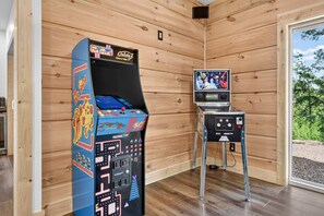 A room with wooden walls and a wooden floor, featuring two arcade machines, one with a colorful design and another with a Star Wars theme. - Blue Ridge Retreat on Wolf Creek - Hot Tub, Game Room, Firepit + EV Charger (Mineral Bluff)