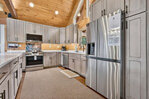 A modern kitchen with stainless steel appliances, wooden cabinets, and a wooden ceiling. - Blue Ridge Retreat on Wolf Creek - Hot Tub, Game Room, Firepit + EV Charger (Mineral Bluff)